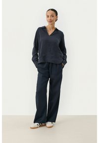 Navy linen blouse with a collar, loose fit, and three-quarter sleeves. Paired with wide-leg navy trousers and light-colored sneakers.