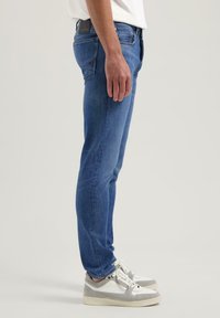 Modri denim kavbojki s slim fit krojem, središnjim pasom, diskretnim izginjanjem in klasičnim pet-pocket dizajnom. Okraskovan z usnjenim oznako.