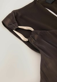 Čierny saténový odev s hladkým povrchom, ktorý má detail z kovu striebornej farby na výstrihu a zhromaždenú látku po stranách.