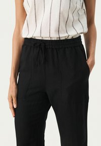 Black linen pants with an elastic waistband and drawstring, featuring two side pockets and a smooth texture.