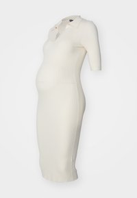 Robe ajustée, longueur genou, en tricot côtelé crème avec un col polo et des manches courtes, conçue pour les vêtements de maternité avec une texture lisse.