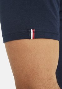 Marineblaue Baumwoll-T-Shirt mit kurzen Ärmeln, mit einem kleinen rot-weißen-blauen gestreiften Akzent nahe dem Saum. Glatte Textur.