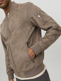 Giacca bomber in suede marrone chiaro con zip frontale, polsini a costine e una tasca con zip sul braccio sinistro. Texture morbida, design casual.