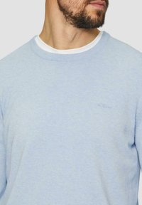 Hellblaues, gestricktes Rundhalsoberteil mit geripptem Kragen. Verfügt über ein dezentes Logo in passender Farbe auf der Brust. Weiche Textur.