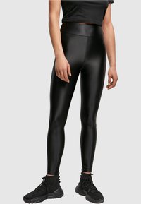 Leggings neri a vita alta realizzati in un materiale lucido e elasticizzato. Silhouette aderente con texture liscia e senza motivi o elementi hardware visibili.