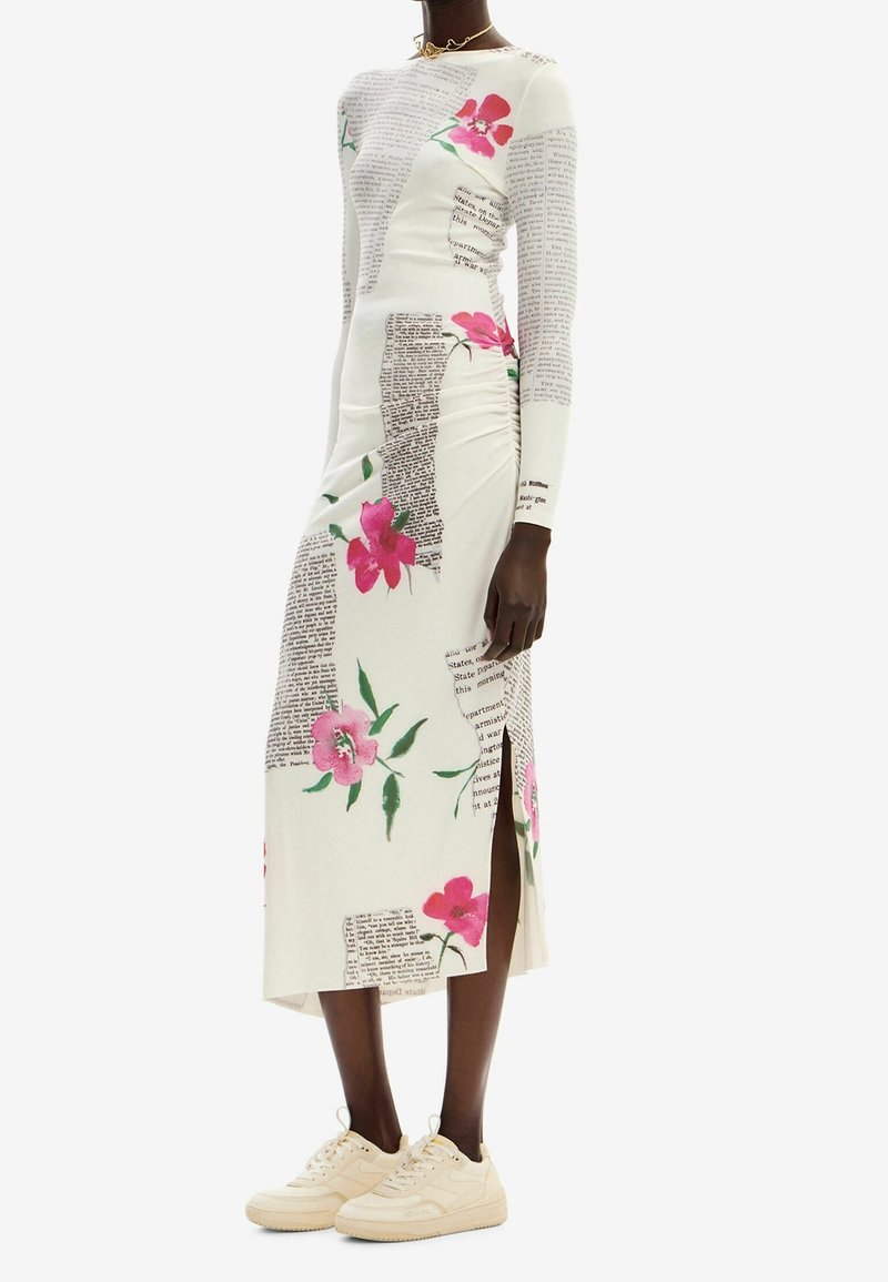 Robe à manches longues blanche avec motifs floraux et impression de texte. Présente une fente sur le côté et des détails froncés. Associée à des baskets de couleur claire.