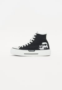 Høyhælte sneakers i svart lerret med hvit gummisåle og lisser. Har grafikk av to figurer med solbriller på siden.