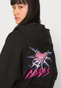 Felpa nera con cappuccio caratterizzata da un design grafico in rosa e blu, con dettagli a raggiera e la parola "ADIDAS" in caratteri in grassetto sul retro.