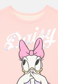 Różowy bawełniany t-shirt z grafiką postaci z kreskówki z różową kokardą, obok której znajduje się słowo „Daisy” w błyszczących srebrnych literach.