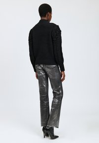 Maglione nero lavorato a maglia con maniche a sbuffo testurizzate, indossato con pantaloni dritti metallici argento e stivali neri con tacco alto.