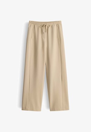 Lichtbeige wijde broek met een elastische tailleband en een trekkoord. Heeft twee voorzakken en een gladde textuur.