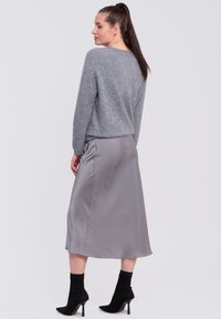 Lichtgrijze, gebreide sweater gecombineerd met een mid-lange, satijnen grijze rok. Zwarte, spitse hoge hakken met geribbelde enkelkousen.