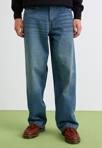 Løse blå denimjeans med falming, fem lommer og rett snitt. Brukt med brune skinnsko med frynse-detaljer.