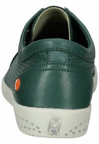 Zielone skórzane buty z perforowanym wzorem, zaokrąglonym obcasem i białą gumową podeszwą. Posiadają okrągły pomarańczowy akcent w pobliżu pięty.