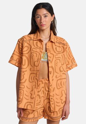 Maglietta arancione a maniche corte con motivi astratti marroni, con chiusura frontale a bottoni e dettaglio in pizzo, abbinata a pantaloncini coordinati.