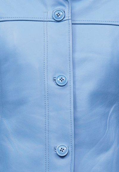 Κοντινό πλάνο σε ανοιχτό μπλε δερμάτινο ένδυμα με κάθετες ραφές και τρία στρογγυλά κουμπιά στο ίδιο χρώμα κατά μήκος του κεντρικού μπροστινού μέρους.