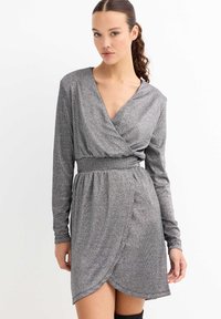 Vestido cruzado gris con mangas largas, escote en V y cintura ajustada. La tela tiene un acabado brillante y texturizado, con un dobladillo hasta la rodilla.
