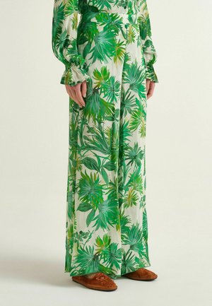Gonna lunga con stampa di foglie tropicali verdi, abbinata a top a maniche lunghe coordinato e scarpe basse ricamate marroni.