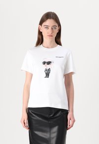 Weißes Baumwoll-T-Shirt mit einer Cartoon-Figur in schwarzen Sonnenbrillen und Anzug, mit "Karl Lagerfeld" über der Grafik aufgedruckt. Normale Passform.