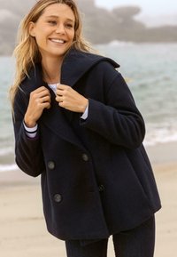 Marineblauwe dubbele-breasted peacoat van een gestructureerde stof, met grote knopen, een brede kraag en een oversized silhouet, gedragen over een gestreept top.