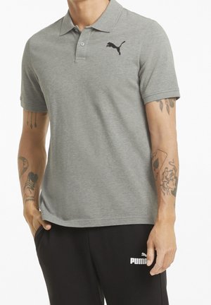 Graues Poloshirt mit einem Kragen und kurzen Ärmeln, versehen mit einem schwarzen Puma-Logo auf der linken Brust. Weiche Stoffstruktur.