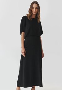 Schwarzes Maxikleid mit kurzen, weiten Ärmeln; glatter Stoff mit einem subtilen Glanz; taillierter Oberteil, fließender Rock und schlichte Silhouette.