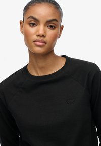 Zwart sweatshirt met een ronde hals, raglanmouwen en geborduurd "Super Dry" logo op de borst. Gladde stof, casual pasvorm.