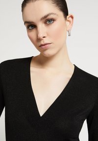 Crna majica s dubokim V-izrezom i dugim rukavima, izrađena od blago sjajne, teksturirane tkanine. Ima glatki izrez i pripijeni siluet.