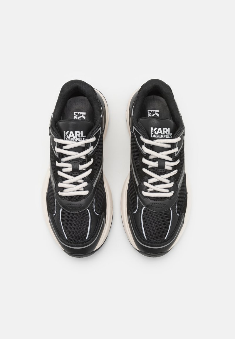 Baskets en mesh noires avec des lacets blancs, dotées d'une épaisse semelle en caoutchouc crème. Logo notable sur la languette et détails cousus sur le dessus.