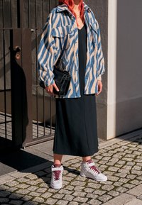 Blå och beige randig fleece-tröja, svart klänning och vita sneakers med burgundyröda accenter, kombinerat med en liten svart handväska.