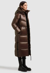 Barna puffertakaró kapucnival, fényes felülettel, párnázott részekkel és cipzáras zsebekkel. Fekete, vastag bokacsizmával párosítva.