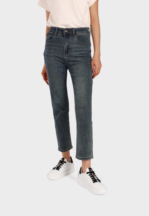 Persona che indossa jeans corti a vita alta di colore blu scuro abbinati a sneakers bianche con suola platform e dettagli neri, e una maglietta bianca.