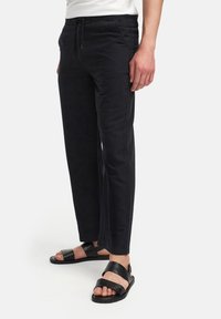 Svarta byxor med avslappnad passform, med elastisk midja, dragsko och sidofickor. Matchas med svarta sandaler med breda remmar.