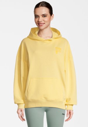 Gul hættetrøje med en frontlomme, afslappet pasform og ribbede manchetter. Har et lille logo på brystet. Bæres med grønne leggings.