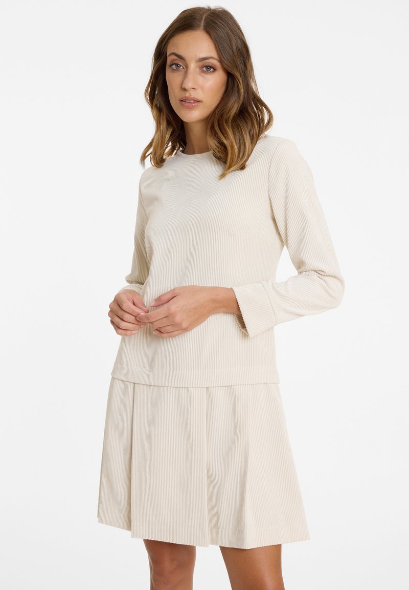 Beiges Rippstrickkleid mit langen Ärmeln; hat eine eng anliegende Oberseite und einen plissierten Rock, der Textur und klare Linien präsentiert.