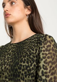 Top com padrão de leopardo verde e preto, com um design texturizado e franzido; mangas bufantes transparentes realçam a aparência fluida do tecido.