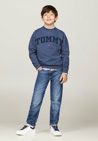 Felpa navy con logo "TOMMY", abbinata a jeans azzurri chiari e sneaker bianche. Design semplice, vestibilità casual e materiale in cotone.