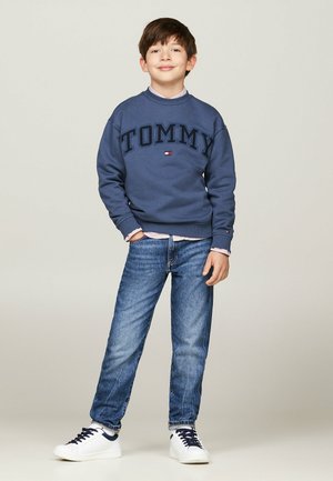 Felpa navy con logo "TOMMY", abbinata a jeans azzurri chiari e sneaker bianche. Design semplice, vestibilità casual e materiale in cotone.