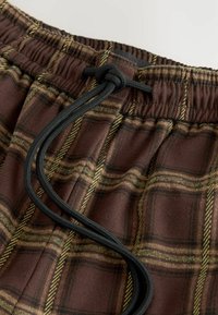 Bruine geruite shorts van zachte stof, met een trekkoordsluiting met zwart koord en gele accenten in het ruitpatroon.