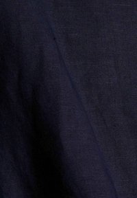 Tissu texturé bleu marine avec un tissage subtil, présentant un léger éclat et une apparence lisse. L'arrière-plan est flou.