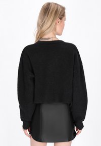 Melna īsā džemperis, izgatavots no mīksta adījuma ar garām, vaļīgām piedurknēm un ribbētu apakšmalu, apvienots ar elegantu melnu ādas minisko. 