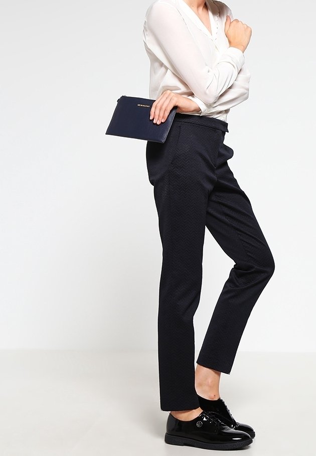 Marinblå mönstrade byxor med rak passform, kombinerade med en lätt blus och svarta blanka skor; håller en mörk clutch.