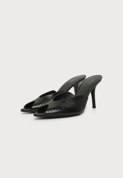 Paire de mules noires à talons hauts avec bouts pointus et surface texturée brillante sur un fond blanc uni.