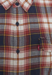 Camicia a quadri rossa, blu navy, gialla e bianca con bottoni, tasca sul petto e un piccolo etichetta rossa del marchio Levi's sul bordo della tasca.