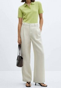 Zelený úpletový polo tričko s texturou, krémové široké kalhoty s vysokým pasem, černé lodičky na podpatku a malá hnědá kabelka.