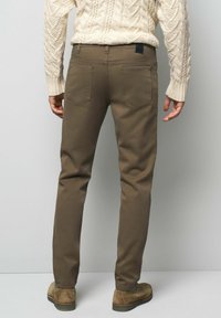 Bruine broeken in een slim-fit ontwerp, gemaakt van een gladde stof. Voorzien van twee achterzakken en een zwart merklabel op de taille.