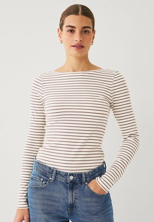 Long-sleeve, fitted top in cream with thin brown stripes. Cotton ribbed texture; boat neckline, worn with blue high-waisted jeans.
