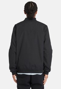 Giubbotto bomber nero con texture liscia, polsini e orlo a costine. Presenta un colletto rialzato e una vestibilità comoda. Nessun logo o motivo visibile.