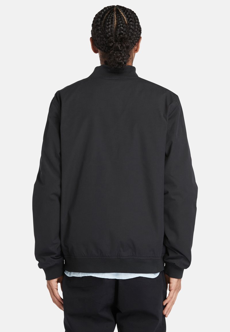 Veste bomber noire avec une texture lisse, des poignets et un ourlet côtelés. Présente un col montant et une coupe décontractée. Aucun logo ou motif visible.