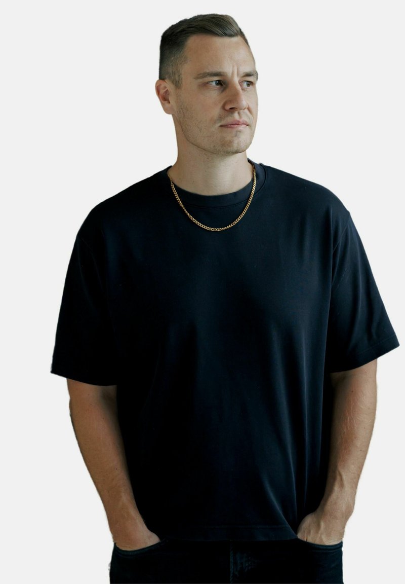 Sort kortærmet T-shirt i afslappet pasform, lavet af blødt bomuld, med rund hals og en glat tekstur. Guld kædeørering som accent.